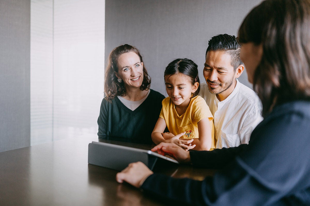 Financial advisor meeting with a family seated at a table, reviewing information together on a tablet in a quiet office setting.