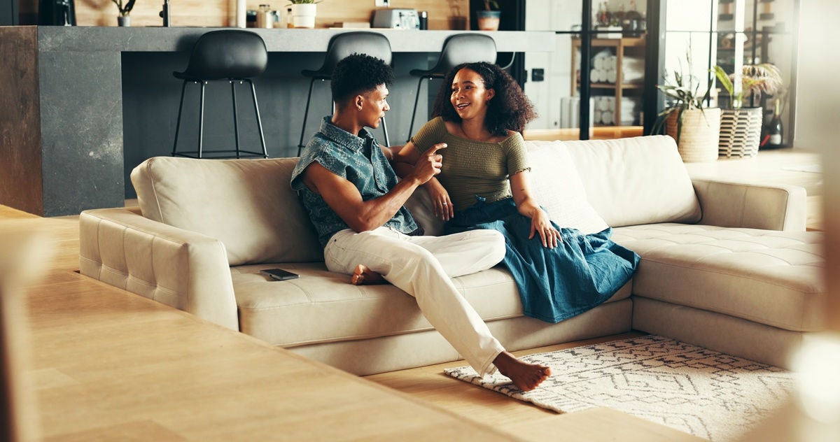 Happy couple, smile and talking in living room in bonding together, relax or peace on couch in home. Woman, man and conversation with healthy communication on weekend as discussion, chatting and love
