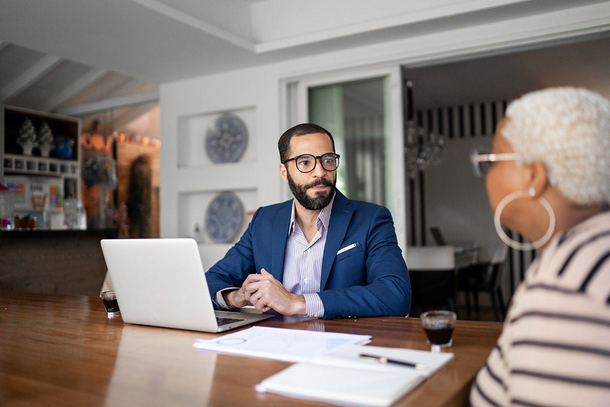 Advisor sitting at a table with a client, discussing documents and working on a laptop in a bright, modern office