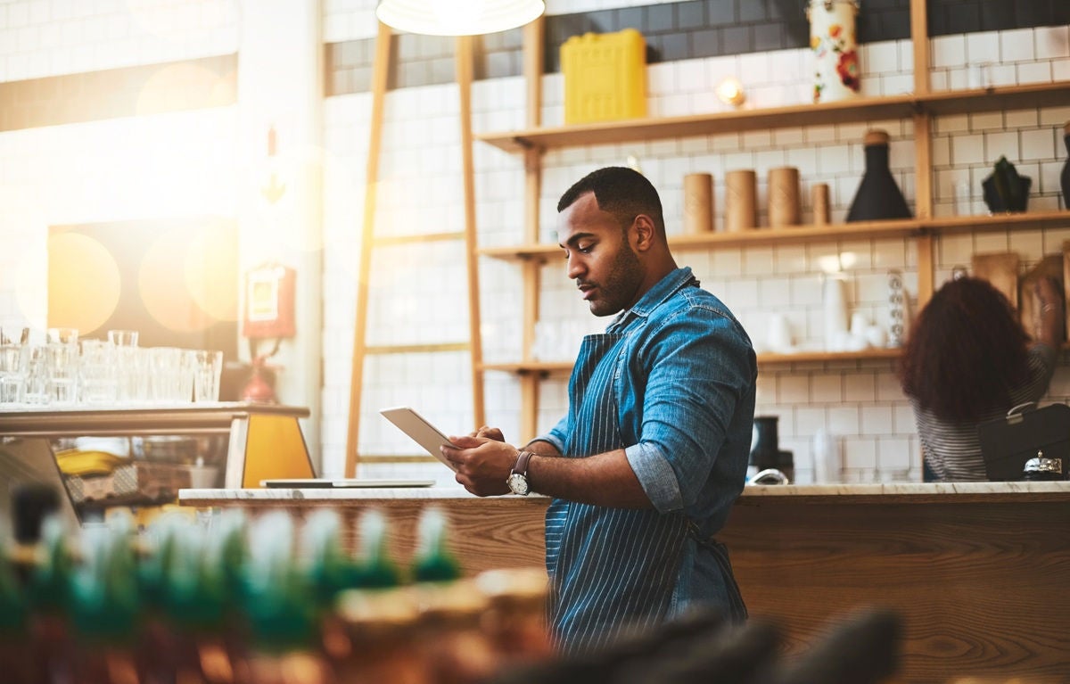 Small business owner reviewing invoices and payment information behind the counter of a cafe.