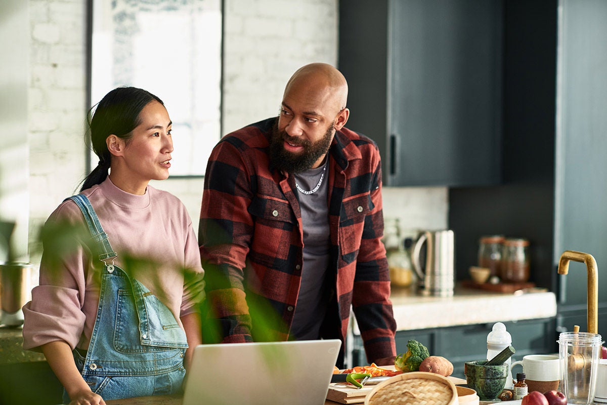 Couple reviewing household finances and budgeting together on laptop in home kitchen